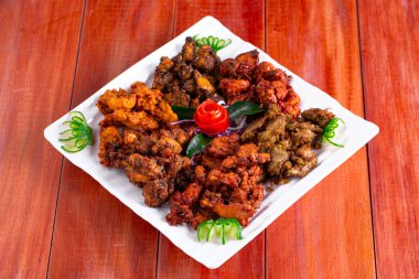 Pakora tavuğu, beyaz kare bir tabakta dizilmiş ve ahşap bir arka planda domates ve salatalıkla süslenmiş üç farklı Pakora çeşidi..