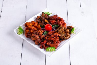 Pakora tavuğu, beyaz bir tabağa dizilmiş ve beyaz bir arka planda domates ve salatalıkla süslenmiş üç farklı Pakora çeşidi..