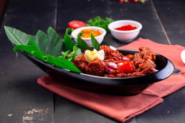 Tavuk Peralan veya tavuk köri, kerala özel tavuk tabağı oval şekilli ve muz yaprağıyla kaplanmış ve çiçek şeklinde yumurta ve soğan aromalı siyah arka planda masa pıhtısıyla kaplanmış siyah bir masa örtüsü ile güzelce düzenlenmiştir.