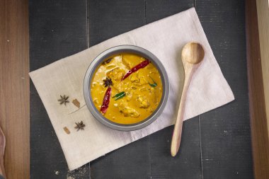 Çiğ muzlu körili tavuk (muz körisi), yeşil muz aromalı baharatlı tavuk ve siyah arka planlı bir mendilin üzerindeki sofra takımında sıralanmış Hint yemeği..