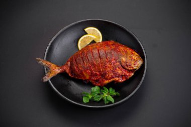 Balık kızartması _ Pomfret kızartması, kişniş yaprağı ve limon dilimleriyle süslenmiş siyah arka planda siyah bir kasede..