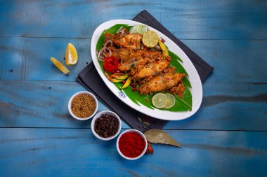 Pomfret masala veya meen pollichadu, baharat kullanan özel kerala yemeği ve muz yaprağıyla kaplanmış, salata ve limon dilimleriyle süslenmiş beyaz desenli arka planda bir sofra takımı..