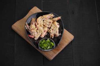 Tereyağlı sarımsaklı karides ya da kremalı sarımsaklı karides, siyah bir sofra takımına yerleştirilmiş, kısmen salata olarak doğranmış, mavi desenli arka planda..