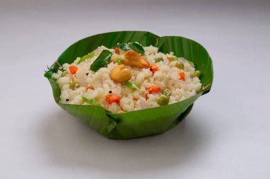 Samolina veya rava 'dan yapılmış upma, Güney Hindistan kahvaltı öğesi muz yaprağından yapılmış bir kasede güzelce düzenlenmiş ve beyaz desenli arka planda kızarmış kaju fıstığı ile süslenmiş..