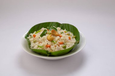 Samolina veya rava 'dan yapılmış upma, Güney Hindistan kahvaltı öğesi muz yaprağından yapılmış bir kasede güzelce düzenlenmiş ve beyaz desenli arka planda kızarmış kaju fıstığı ile süslenmiş..