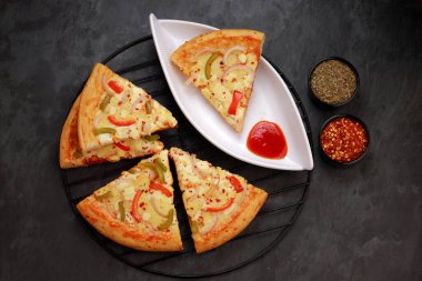 Pizza _ 3 katmanlı peynirli pizza, kırmızı, yeşil ve sarı dolmalık biber, soğan ve mozzarella peyniri, ince hamur dilimleri, siyah ızgarada güzelce yerleştirilmiş ve beyaz masa üzerine asingle dilimleri, kırmızı biber taneleri ve origano ile yerleştirilmiş.
