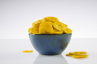 Kurutulmuş muz cipsi ya da muz waffle 'ı, beyaz desenli arka planda, su kırsal seramik kasede güzelce dizilmiş..