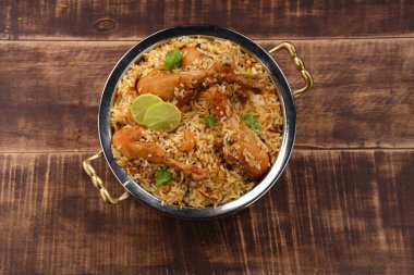 Dum tavuklu biryani, Kerala-Thalassery biryani 'nin yakın plan görüntüsü masala ve sarıyla karıştırılmış bakır servis kasesine yerleştirilmiş ve ahşap desenli arka planda limon dilimleri ile süslenmiş..