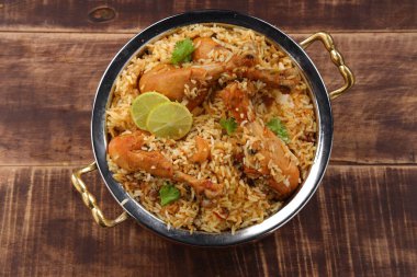 Dum tavuklu biryani, Kerala-Thalassery biryani 'nin yakın plan görüntüsü masala ve sarıyla karıştırılmış bakır servis kasesine yerleştirilmiş ve ahşap desenli arka planda limon dilimleri ile süslenmiş..