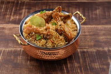 Dum tavuklu biryani, Kerala-Thalassery biryani 'nin yakın plan görüntüsü masala ve sarıyla karıştırılmış bakır servis kasesine yerleştirilmiş ve ahşap desenli arka planda limon dilimleri ile süslenmiş..
