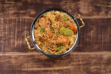 Dum tavuklu biryani, Kerala-Thalassery biryani 'nin yakın plan görüntüsü masala ve sarıyla karıştırılmış bakır servis kasesine yerleştirilmiş ve ahşap desenli arka planda limon dilimleri ile süslenmiş..