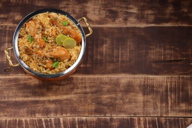 Dum tavuklu biryani, Kerala-Thalassery biryani 'nin yakın plan görüntüsü masala ve sarıyla karıştırılmış bakır servis kasesine yerleştirilmiş ve ahşap desenli arka planda limon dilimleri ile süslenmiş..