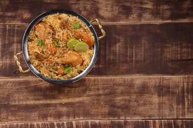 Dum tavuklu biryani, Kerala-Thalassery biryani 'nin yakın plan görüntüsü masala ve sarıyla karıştırılmış bakır servis kasesine yerleştirilmiş ve ahşap desenli arka planda limon dilimleri ile süslenmiş..