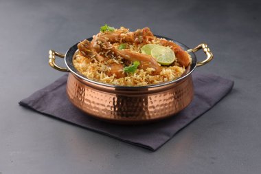 Dum tavuklu biryani, Kerala-Thalassery biryani 'nin yakın plan görüntüsü masala ve sarıyla karıştırılmış bakır servis kasesine yerleştirilmiş ve grafit desenli ve gri arkaplanlı limon dilimleri ile süslenmiş..