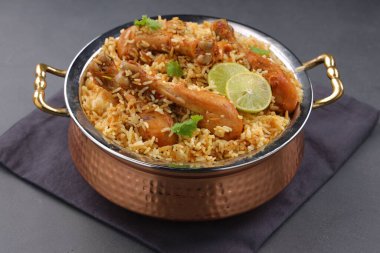 Dum tavuklu biryani, Kerala-Thalassery biryani 'nin yakın plan görüntüsü masala ve sarıyla karıştırılmış bakır servis kasesine yerleştirilmiş ve grafit desenli ve gri arkaplanlı limon dilimleri ile süslenmiş..