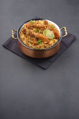 Dum tavuklu biryani, Kerala-Thalassery biryani 'nin yakın plan görüntüsü masala ve sarıyla karıştırılmış bakır servis kasesine yerleştirilmiş ve grafit desenli ve gri arkaplanlı limon dilimleri ile süslenmiş..