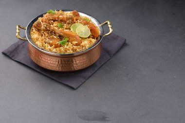 Dum tavuklu biryani, Kerala-Thalassery biryani 'nin yakın plan görüntüsü masala ve sarıyla karıştırılmış bakır servis kasesine yerleştirilmiş ve grafit desenli ve gri arkaplanlı limon dilimleri ile süslenmiş..