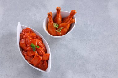 Taze kişniş ve nane yaprağı ile süslenmiş beyaz seramik sofra takımına yerleştirilmiş çiğ tavuk kübü ve bacakları gri desenli arka plana yerleştiriliyor..