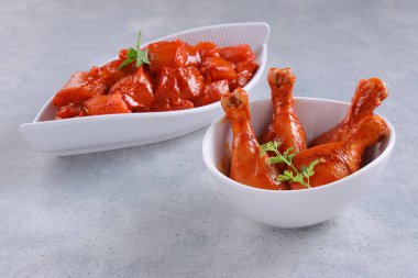 Taze kişniş ve nane yaprağı ile süslenmiş beyaz seramik sofra takımına yerleştirilmiş çiğ tavuk kübü ve bacakları gri desenli arka plana yerleştiriliyor..