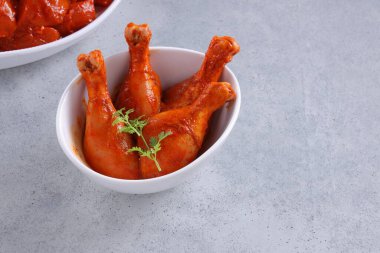 Taze kişniş ve nane yaprağı ile süslenmiş beyaz seramik sofra takımına yerleştirilmiş çiğ tavuk kübü ve bacakları gri desenli arka plana yerleştiriliyor..