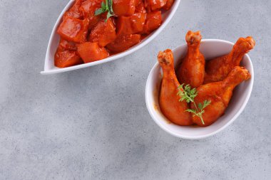 Taze kişniş ve nane yaprağı ile süslenmiş beyaz seramik sofra takımına yerleştirilmiş çiğ tavuk kübü ve bacakları gri desenli arka plana yerleştiriliyor..