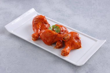 Çiğ terbiye edilmiş tavuk bacağı ya da çubuklar beyaz seramik sofra takımına yerleştirilmiş taze kişniş yaprağı ile süslenmiş gri dokulu arka plana yerleştirilmiş..