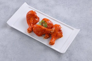 Çiğ terbiye edilmiş tavuk bacağı ya da çubuklar beyaz seramik sofra takımına yerleştirilmiş taze kişniş yaprağı ile süslenmiş gri dokulu arka plana yerleştirilmiş..