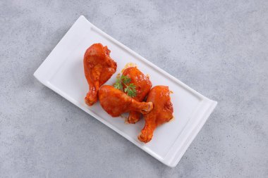 Çiğ terbiye edilmiş tavuk bacağı ya da çubuklar beyaz seramik sofra takımına yerleştirilmiş taze kişniş yaprağı ile süslenmiş gri dokulu arka plana yerleştirilmiş..