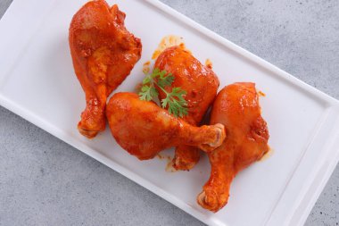 Çiğ terbiye edilmiş tavuk bacağı ya da çubuklar beyaz seramik sofra takımına yerleştirilmiş taze kişniş yaprağı ile süslenmiş gri dokulu arka plana yerleştirilmiş..