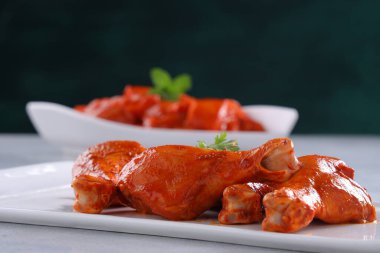 Çiğ terbiye edilmiş tavuk kübü ve bacakları ya da beyaz bir seramik sofra takımına yerleştirilmiş bagetler. Taze kişniş yaprağıyla süslenmiş ve gri beyaz desenli arka plana yerleştirilmiş..