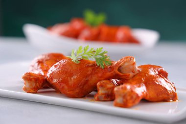 Çiğ terbiye edilmiş tavuk kübü ve bacakları ya da beyaz bir seramik sofra takımına yerleştirilmiş bagetler. Taze kişniş yaprağıyla süslenmiş ve gri beyaz desenli arka plana yerleştirilmiş..