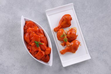 Çiğ terbiye edilmiş tavuk küpler ve bacaklar veya beyaz seramik sofra takımlarına yerleştirilmiş taze kişniş yaprağı ve nane yaprağı ile süslenmiş gri beyaz desenli arka plan üzerine yerleştirilmiş..