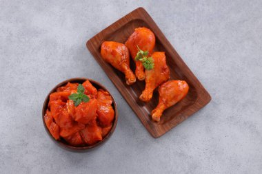 Çiğ terbiye edilmiş tavuk kübü ve bacakları ahşap bir sofra takımına yerleştirilmiş taze kişniş ve nane yaprağı ile süslenmiş gri beyaz desenli arka plana yerleştiriliyor..