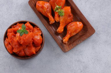 Çiğ terbiye edilmiş tavuk kübü ve bacakları ahşap bir sofra takımına yerleştirilmiş taze kişniş ve nane yaprağı ile süslenmiş gri beyaz desenli arka plana yerleştiriliyor..