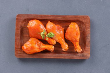 Çiğ terbiye edilmiş tavuk bacağı ya da ahşap bir zemine yerleştirilmiş bagetler. Taze kişniş yaprağıyla süslenmiş. Gri desenli arka plan üzerine yerleştirilmiş..