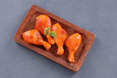 Çiğ terbiye edilmiş tavuk bacağı ya da ahşap bir zemine yerleştirilmiş bagetler. Taze kişniş yaprağıyla süslenmiş. Gri desenli arka plan üzerine yerleştirilmiş..