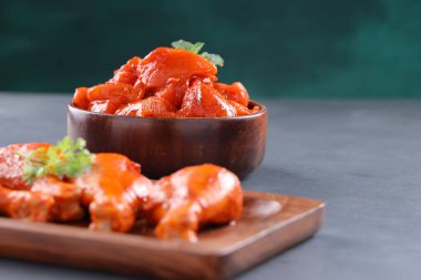 Çiğ terbiye edilmiş tavuk küpler ve bacaklar veya ahşap sofra takımına yerleştirilmiş taze kişniş ve nane yaprağı ile süslenmiş ve gri desenli arka plana yerleştirilmiş, seçici odaklı..