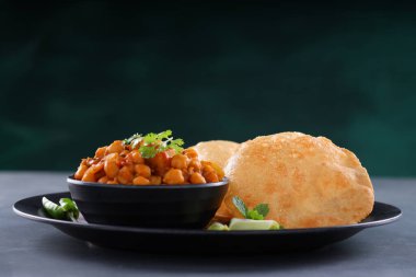 Hint kahvaltısı _ Poori ile nohut chana masala körisi, lezzetli Hint yemeği her amaçlı buğday unu kullanılarak yapılır ki bu da gri desenli arka planda siyah bir tabakta sıralanır.