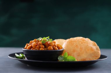 Hint kahvaltısı _ Poori ile nohut chana masala körisi, lezzetli Hint yemeği her amaçlı buğday unu kullanılarak yapılır ki bu da gri desenli arka planda siyah bir tabakta sıralanır.