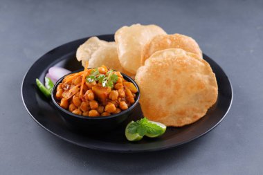 Hint kahvaltısı _ Poori ile nohut chana masala körisi, lezzetli Hint yemeği her amaçlı buğday unu kullanılarak yapılır ki bu da gri desenli arka planda siyah bir tabakta sıralanır.