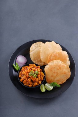 Hint kahvaltısı _ Puri ile nohut chana masala körisi, lezzetli Hint yemeği her amaçlı buğday unu kullanılarak yapılır ki bunlar siyah tabakta, gri desenli arka plan, üst görünüm ile sıralanır.