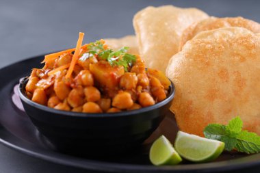 Hint kahvaltısı _ Poori ile nohut chana masala körisi, lezzetli Hint yemeği her amaçlı buğday unu kullanılarak yapılır ki bu da gri desenli arka planda siyah bir tabakta sıralanır.