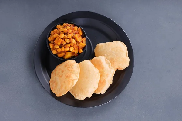 Indian breakfast _Puri with chickpea chana masala curry,tasty indian dish made using all purpose wheat flour which is arranged in a black plate with grey textured background,topview.