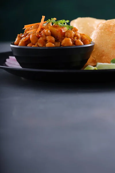 Indian breakfast _Poori with chickpea chana masala curry,tasty indian dish made using all purpose wheat flour which is arranged in a black plate with textured background.
