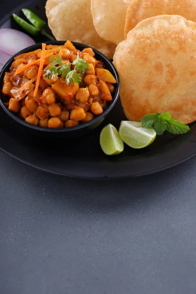 Indian breakfast _Poori with chickpea chana masala curry,tasty indian dish made using all purpose wheat flour which is arranged in a black plate with grey textured background.