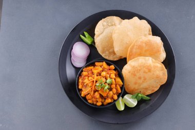 Hint kahvaltısı _ Poori ile nohut chana masala körisi, lezzetli Hint yemeği her amaçlı buğday unu kullanılarak yapılır ki bunlar siyah tabakta, gri desenli arka plan, üst görünüm ile sıralanır.