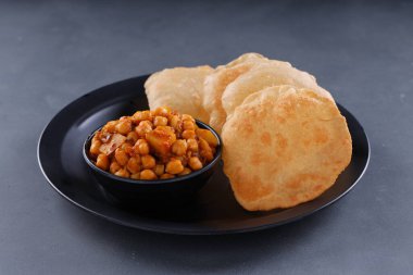 Hint kahvaltısı _ Poori ile nohut chana masala körisi, lezzetli Hint yemeği her amaçlı buğday unu kullanılarak yapılır ki bu da gri desenli arka planda siyah bir tabakta sıralanır.