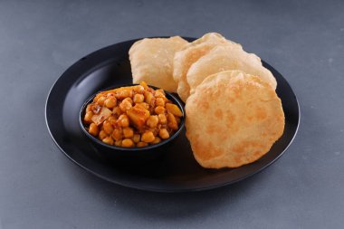 Hint kahvaltısı _ Poori ile nohut chana masala körisi, lezzetli Hint yemeği her amaçlı buğday unu kullanılarak yapılır ki bu da gri desenli arka planda siyah bir tabakta sıralanır.