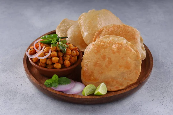 Indian breakfast _Poori with chickpea chana masala curry,tasty indian dish made using all purpose wheat flour which is arranged in a wooden plate with  light grey textured background.