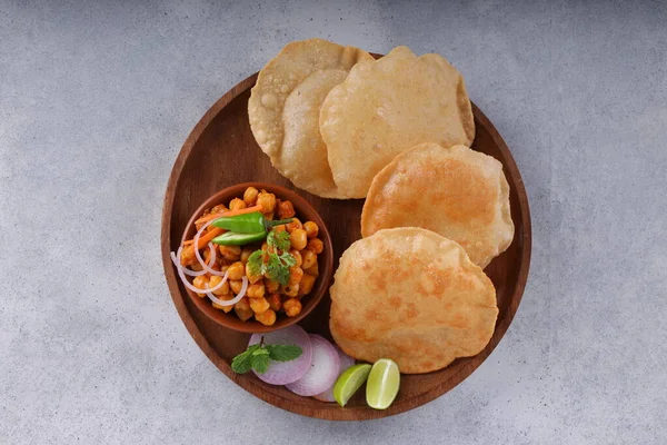 Indian breakfast _Poori with chickpea chana masala curry,tasty indian dish made using all purpose wheat flour which is arranged in a wooden plate with  light grey textured background.